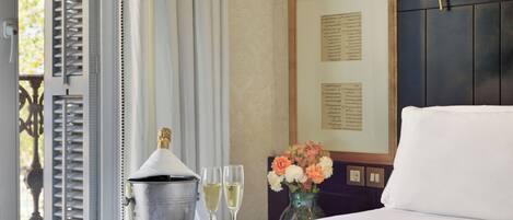 A hotel room with a bed, a tray with a champagne bucket, glasses, and a floral arrangement.