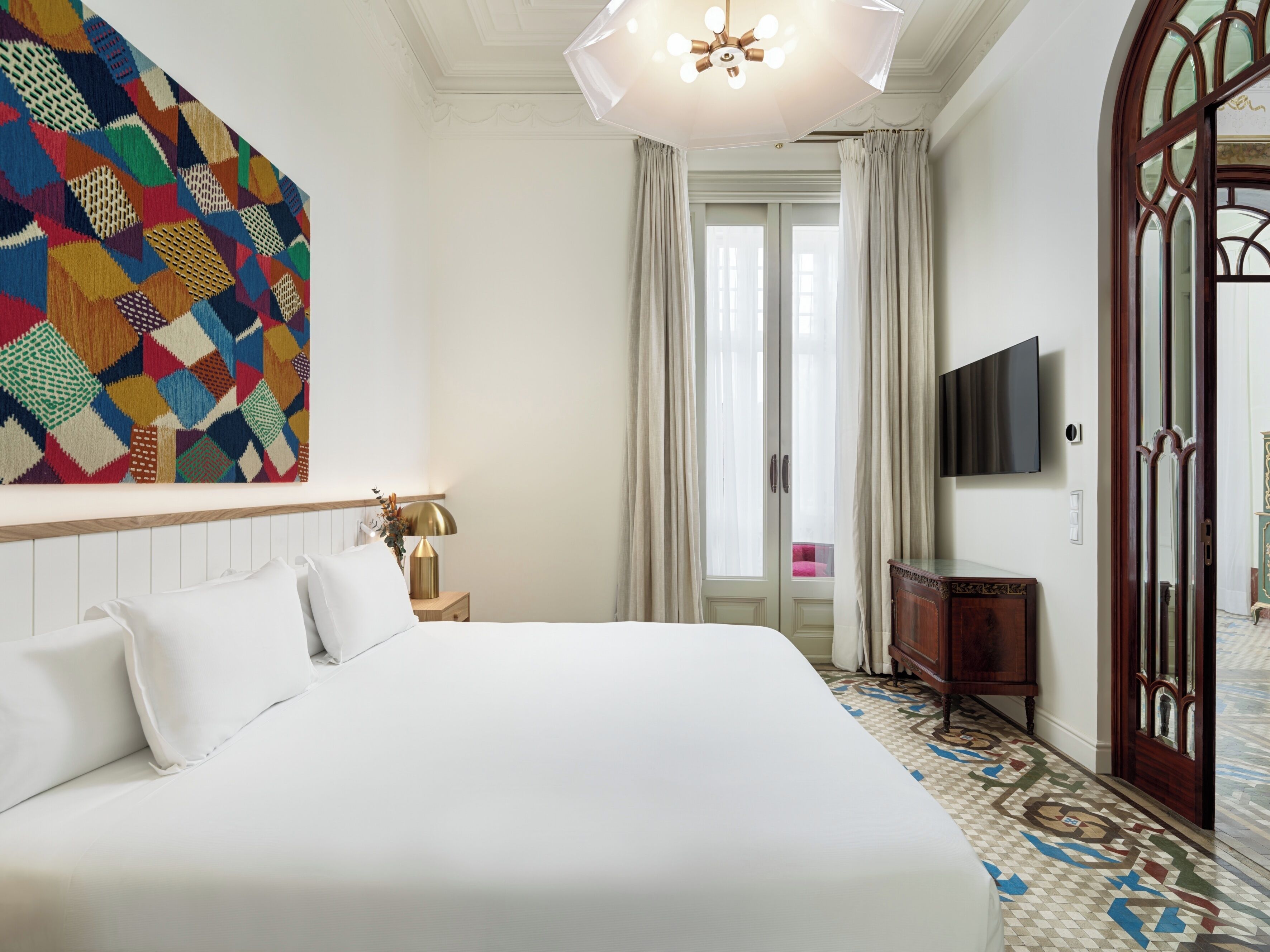A hotel room with a large bed, a television, a wooden cabinet, and a colorful abstract painting on the wall.