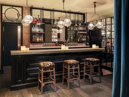 Una zona de bar con taburetes de madera, un espejo y estantes llenos de botellas de licor.