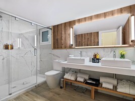 Uma casa de banho moderna com cabine de chuveiro em vidro, duas pias, sanita e toucador com toalhas e produtos de higiene pessoal.