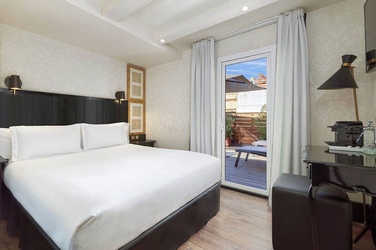 Une chambre d’hôtel avec un grand lit, un bureau avec une chaise, une lampe et une vue sur l’extérieur.