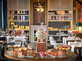 A breakfast buffet with various pastries and desserts, a large glass jar of colorful candies, and neatly arranged tables and chairs.
