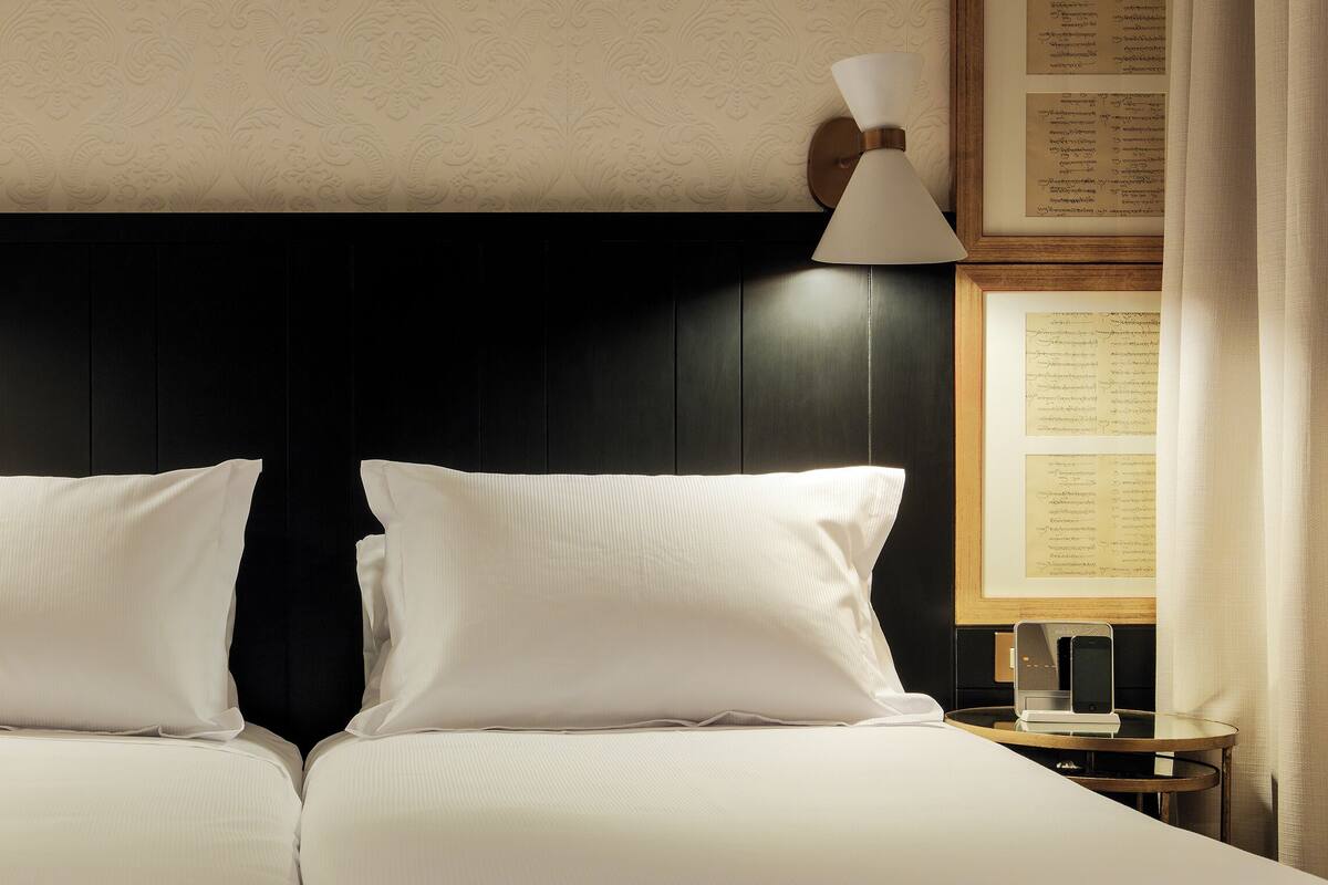 Un lit double avec du linge de lit blanc, deux tables de chevet avec des lampes et des documents encadrés accrochés aux murs.