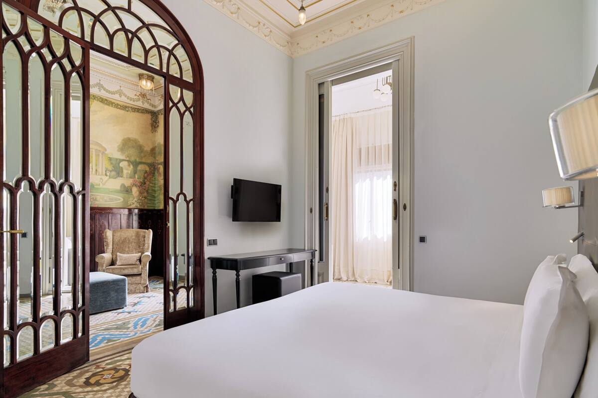 Une chambre d’hôtel avec un grand lit, un bureau, une chaise, une télévision et un miroir décoratif.