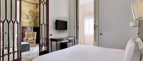 Habitación de hotel con una cama grande, un escritorio, una silla, un televisor y un espejo decorativo.