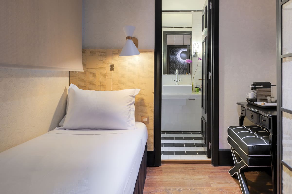 Une chambre d’hôtel comprenant un lit, une table de chevet, un miroir, un lavabo et un petit coin salon.