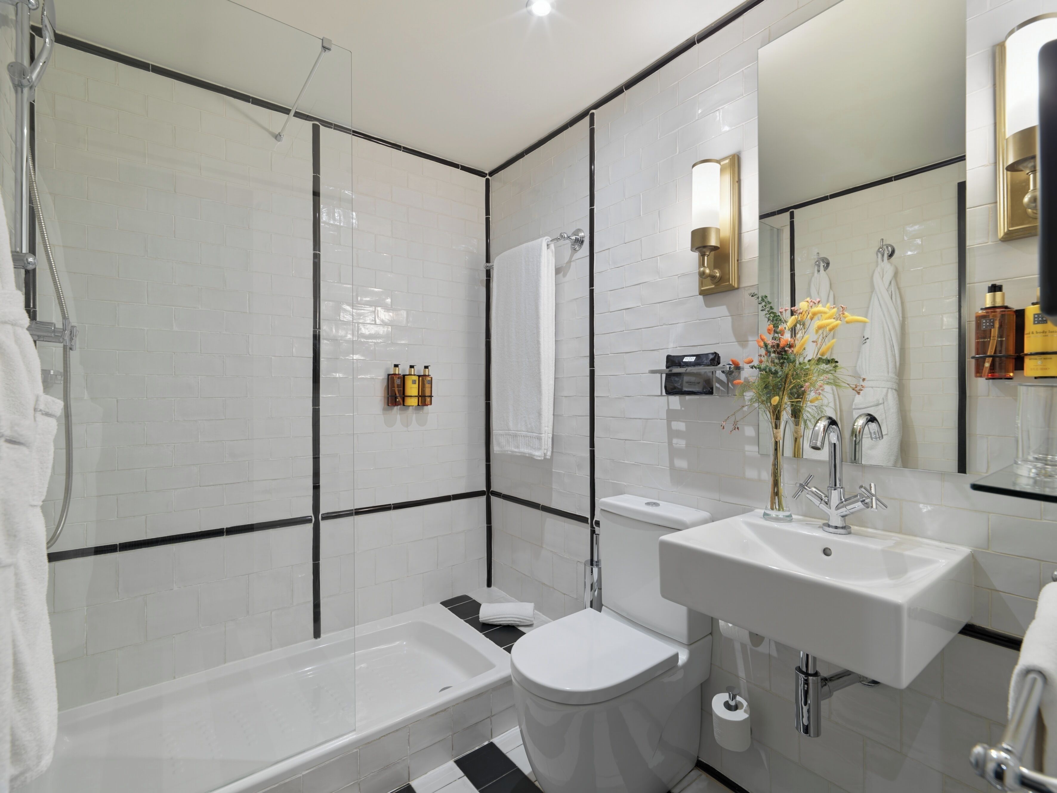 Een moderne badkamer met bad, toilet en wastafel, met witte tegels en een glazen douchecabine.