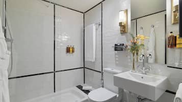 Een moderne badkamer met bad, toilet en wastafel, met witte tegels en een glazen douchecabine.