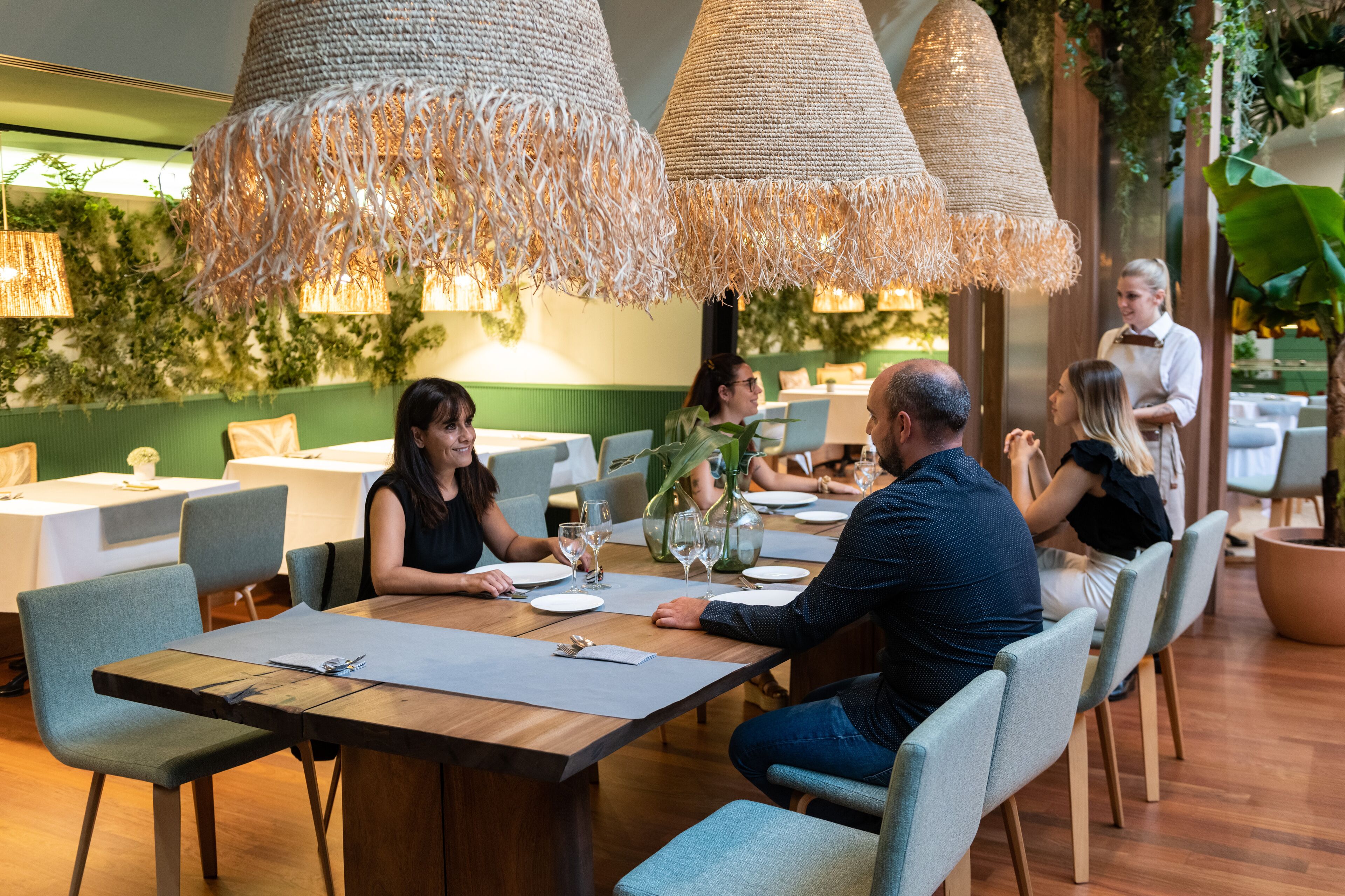 Un restaurante con mesas de madera, sillas azul claro y lámparas colgantes tejidas.