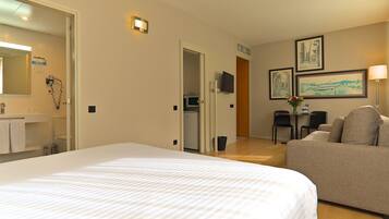 A hotel room with a large bed, a sofa, a desk with a chair, a TV, and artwork on the wall.