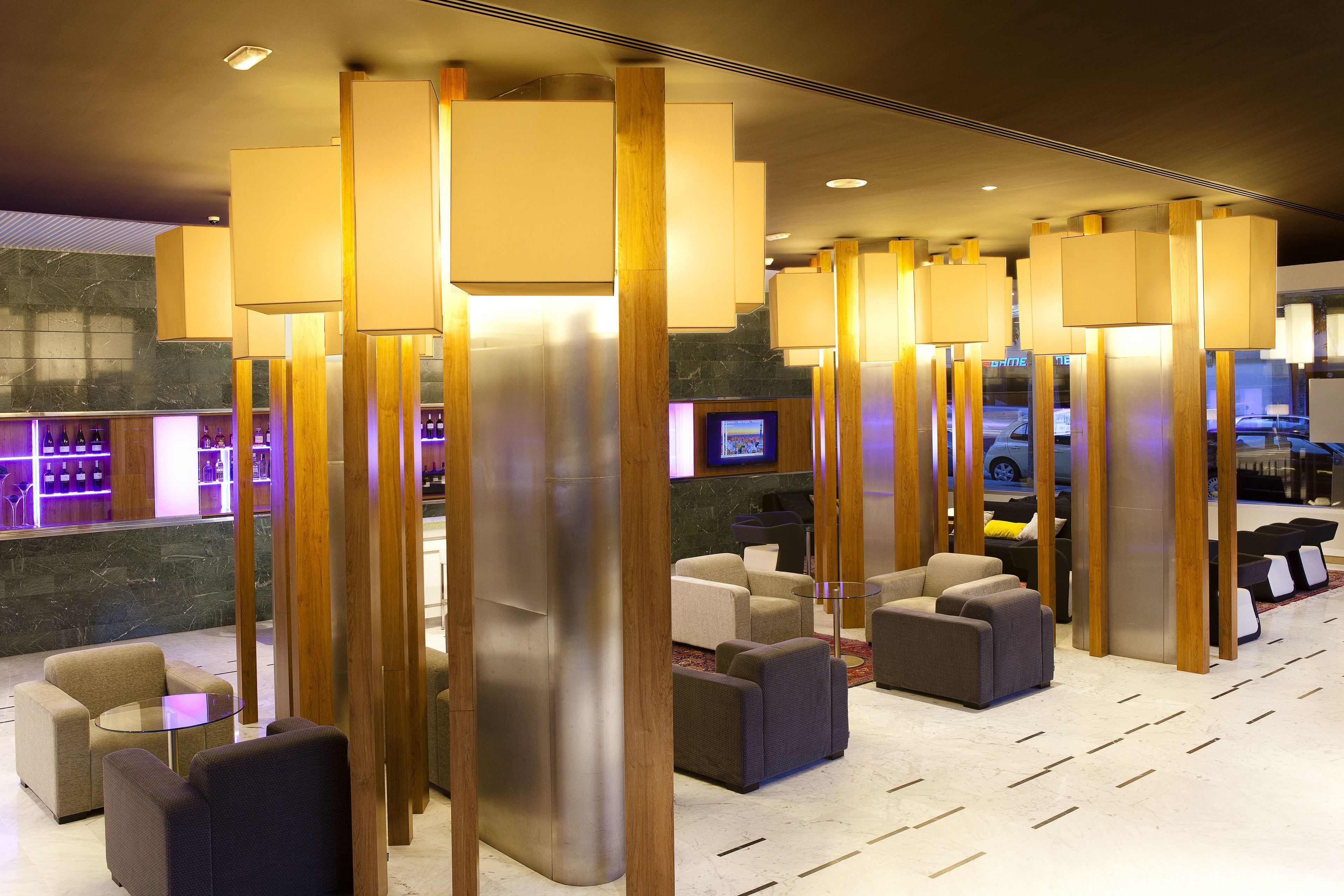Un vestíbulo moderno con altas columnas de madera, asientos cómodos, una zona de bar y una pantalla de televisión.