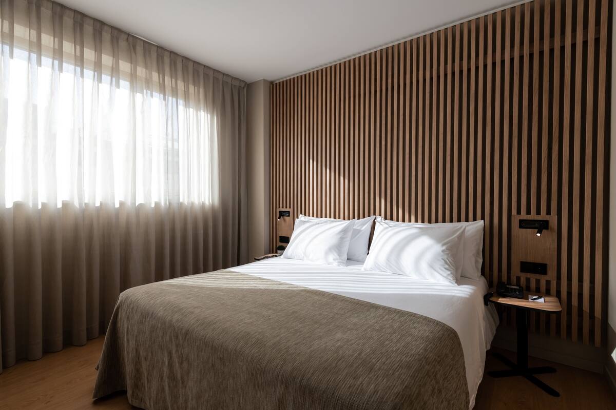 A hotel room with a large bed, a bedside table, and a wall with vertical wooden slats.
