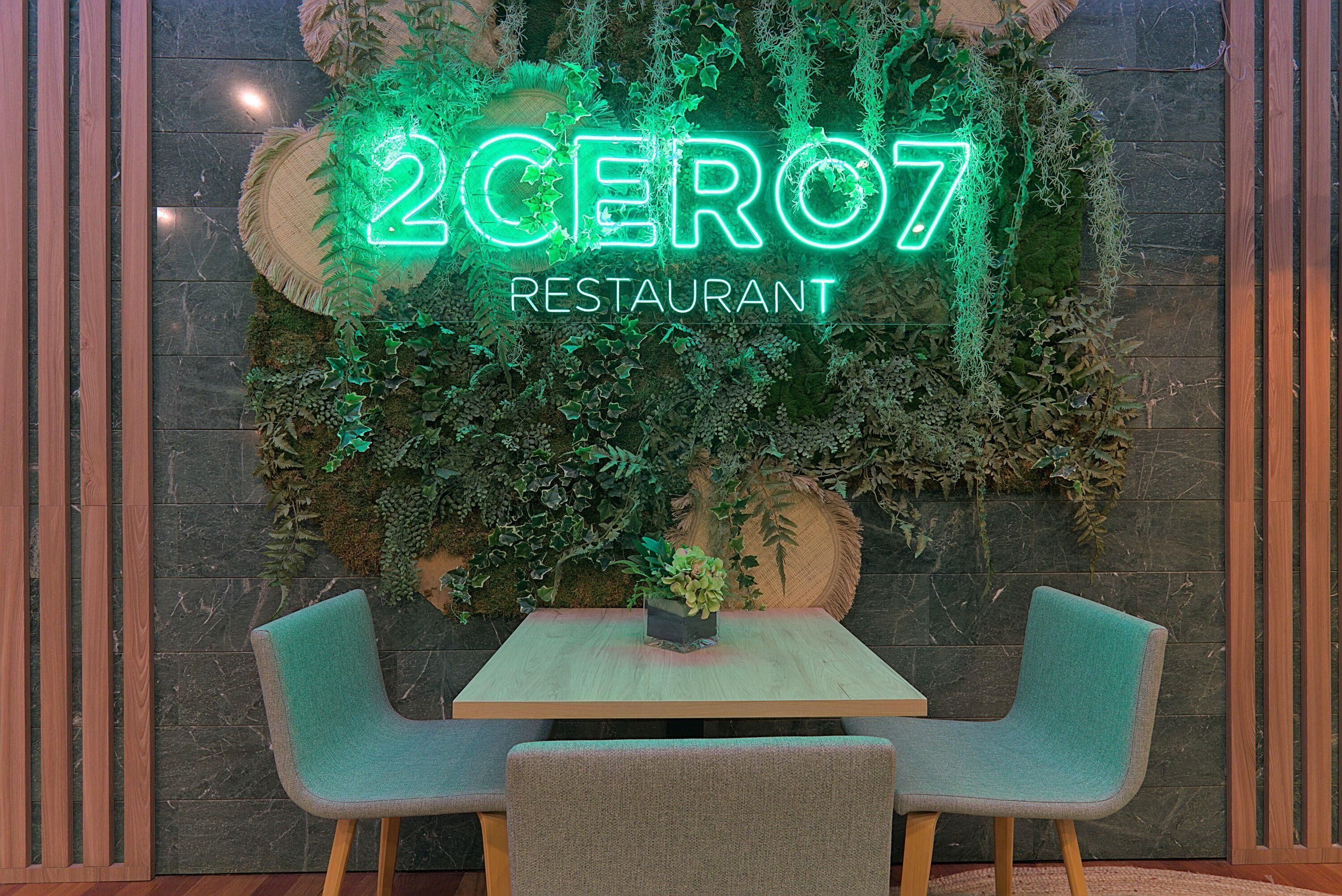 Interior de un restaurante con un letrero de neón, una mesa de madera y dos sillas.