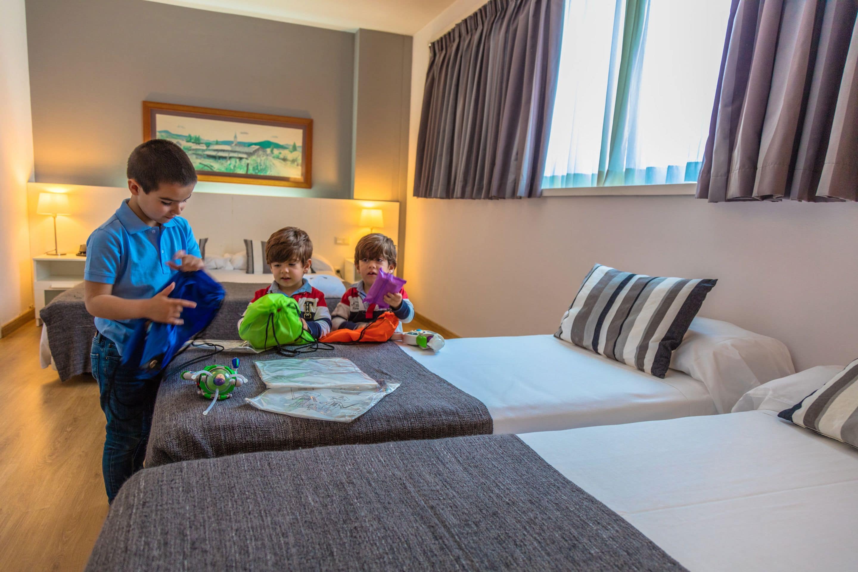 A hotel room with a bed, a sofa, and a table with children's toys and a map.