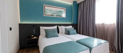 Habitación de hotel con dos camas, una mesita de noche, un cuadro en la pared y una ventana con cortinas.