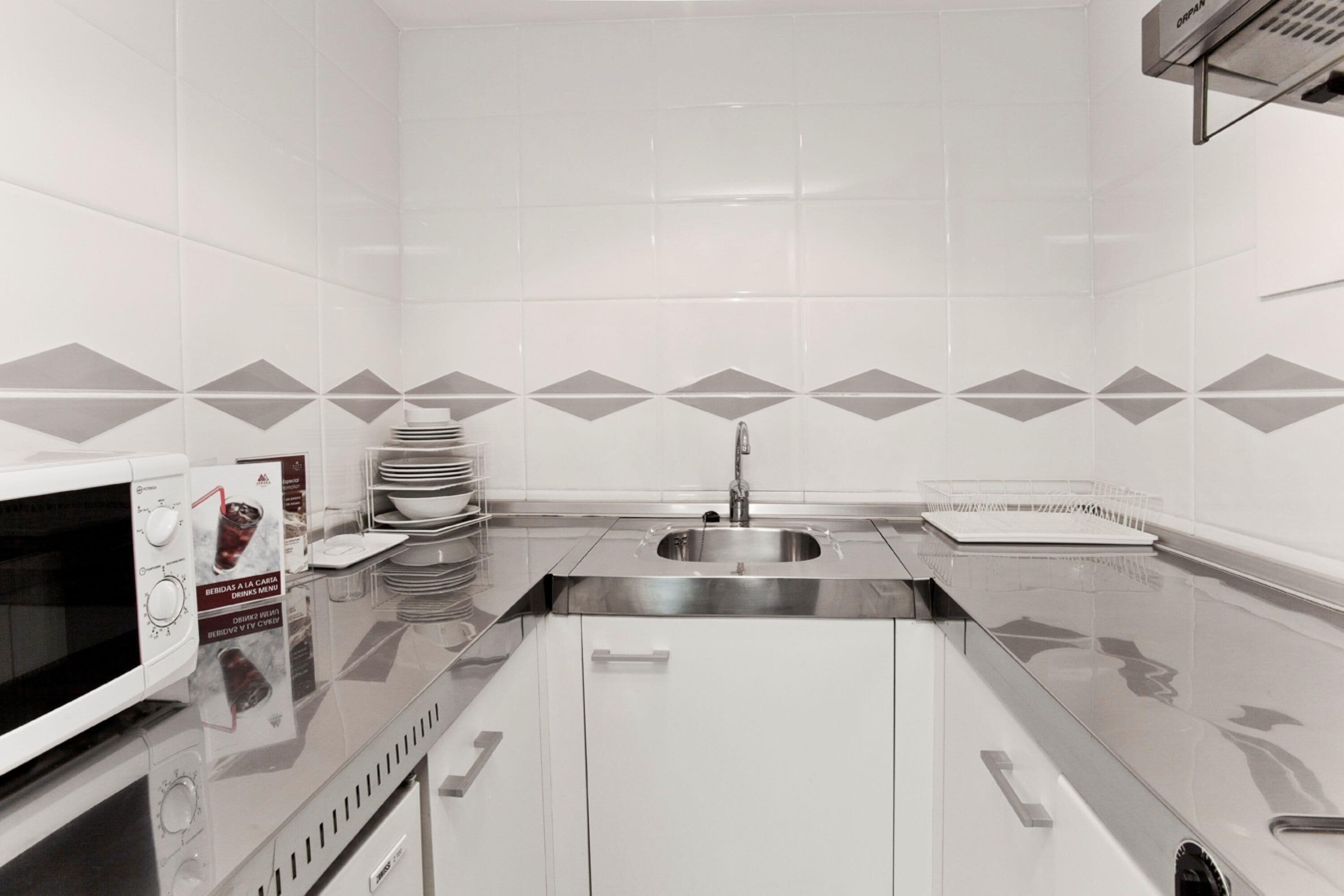 Une cuisine moderne avec des meubles blancs, un évier en acier inoxydable et un four à micro-ondes.