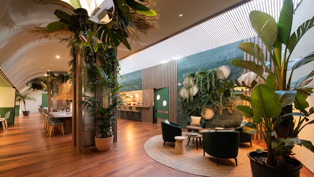 A spacious indoor area with wooden flooring, green seating, and various potted plants. - Aparthotel Atenea Barcelona (Barcelona)
