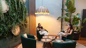 A modern lounge area with green upholstered chairs, a round glass table, and a large potted plant. - Aparthotel Atenea Barcelona (Barcelona)