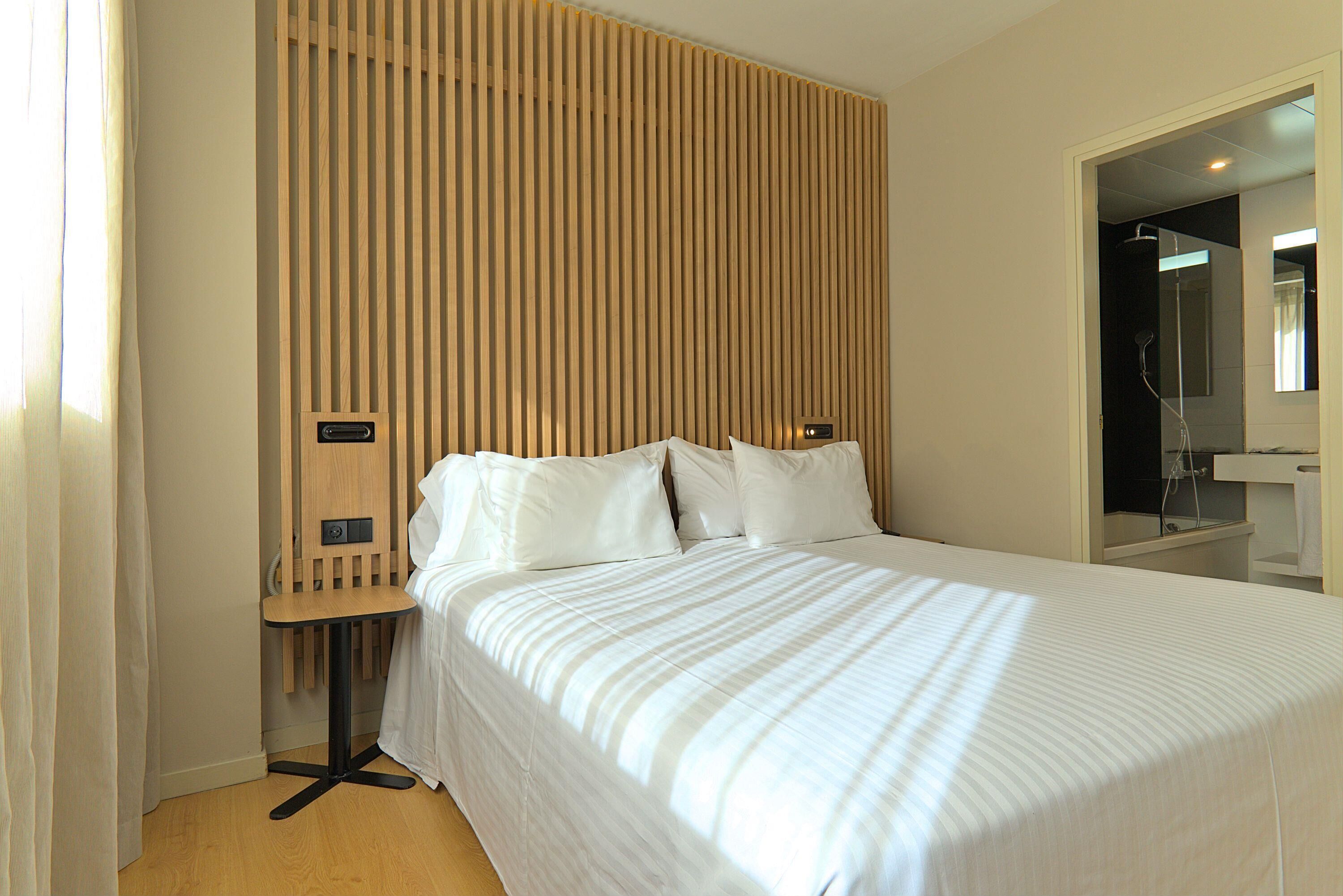 Une chambre d’hôtel avec un lit, un mur recouvert de panneaux en bois, une petite table et un espace douche.