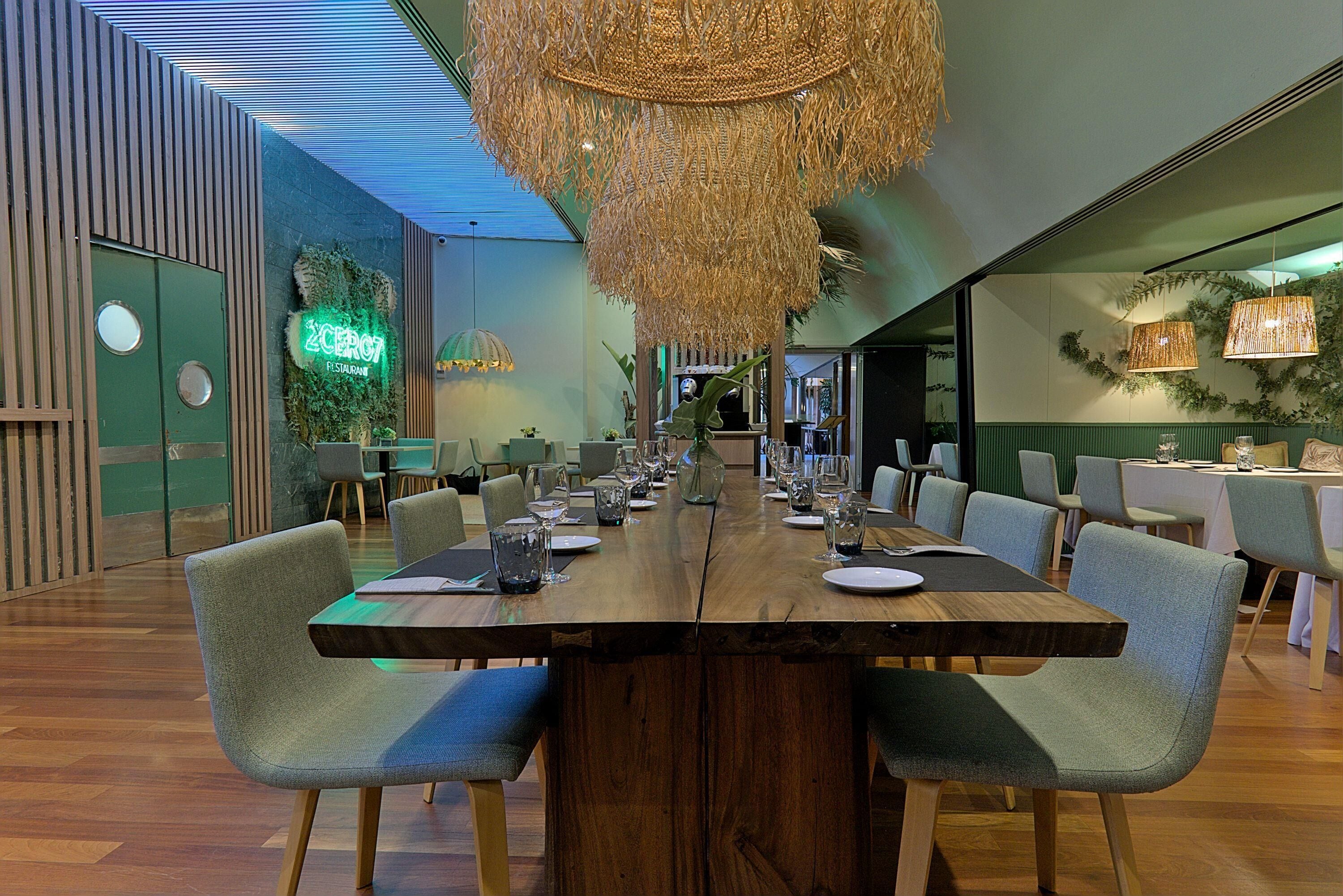 Un ristorante con un lungo tavolo di legno apparecchiato per la cena, circondato da sedie imbottite.