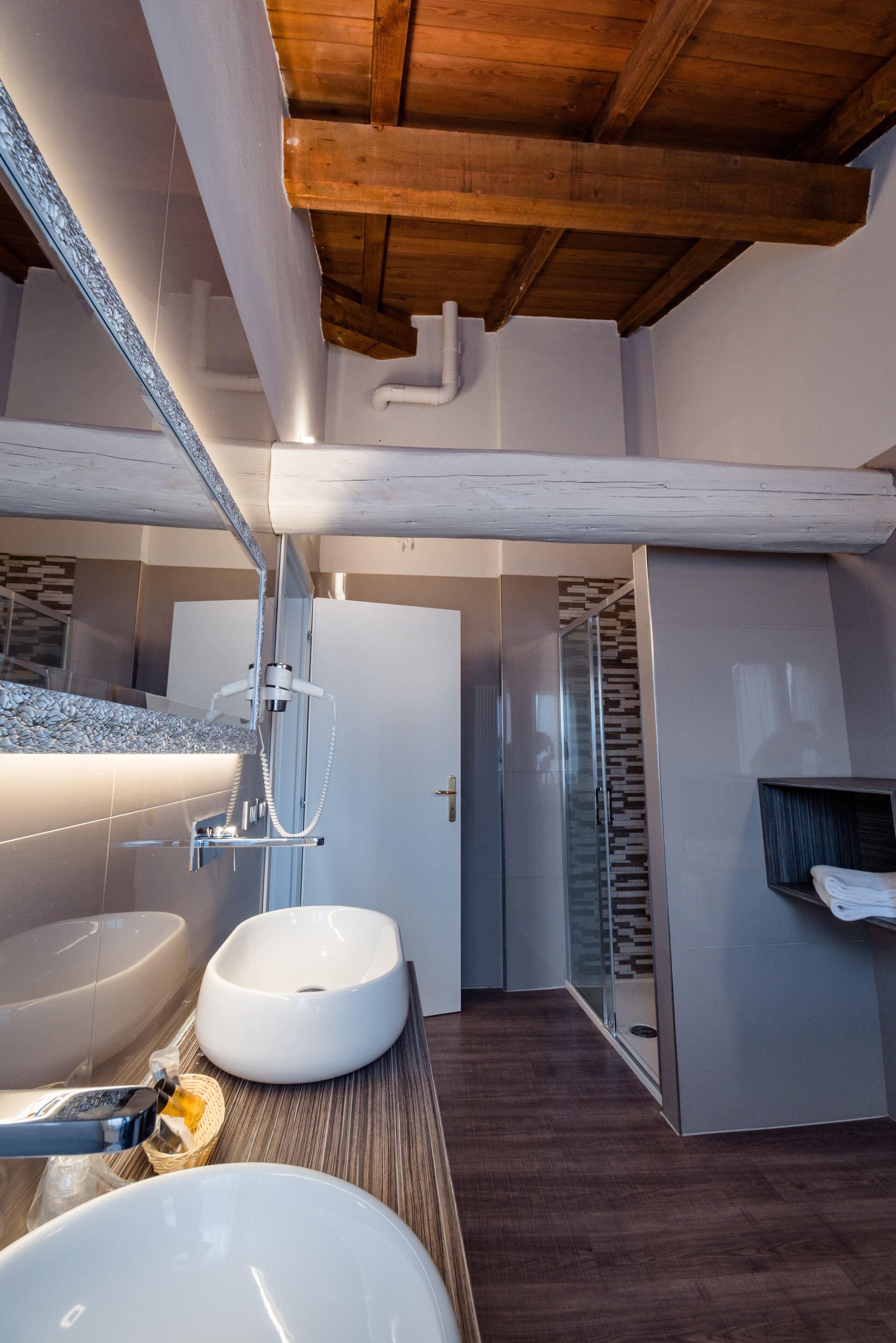 A modern bathroom with a wooden ceiling, a large mirror, two sinks, and a glass shower enclosure.