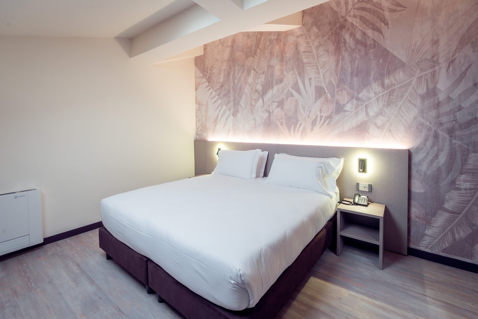 A modern hotel room with a large bed, a nightstand, and a wall-mounted light.