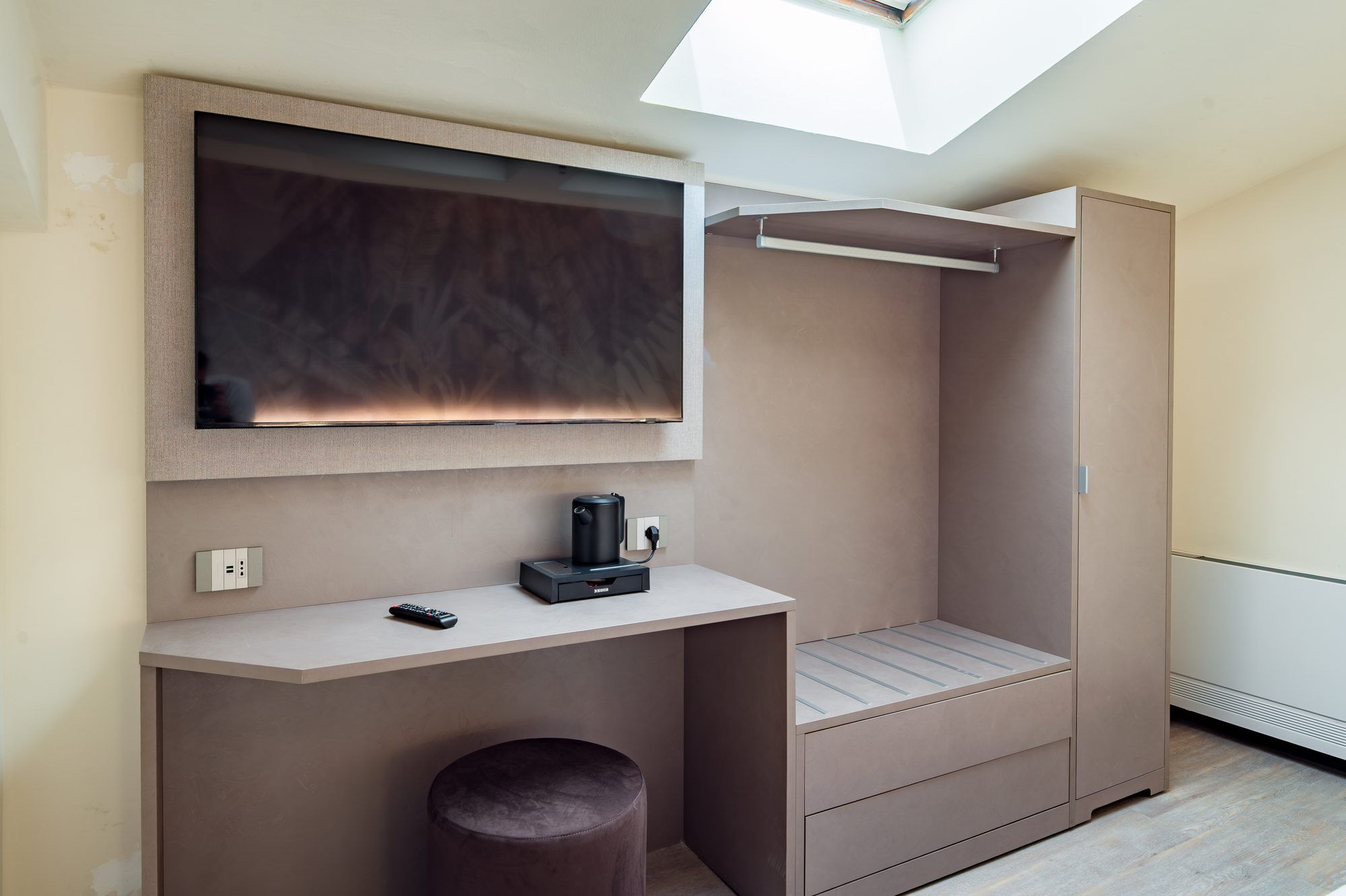 Una habitación moderna y compacta con televisión integrada, una cafetera pequeña y un banco.