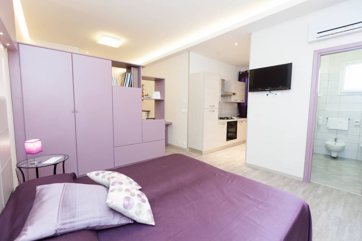 Una camera da letto con un letto, un armadio, un comodino con una lampada e un bagno con lavandino e water.