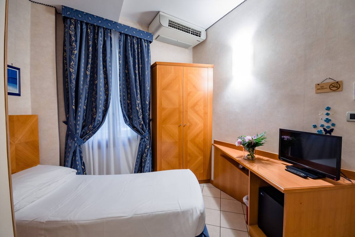 Una camera d'albergo con un letto, un armadio in legno, una scrivania con televisore e un condizionatore d'aria.