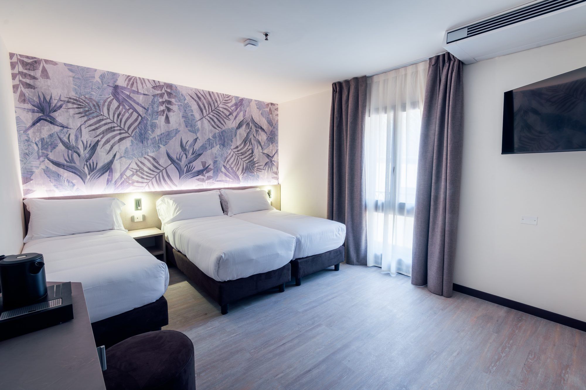Ein Hotelzimmer mit zwei Betten, einem Flachbildfernseher, einer Kaffeemaschine und einem großen Wandteppich.