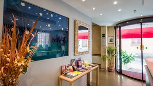 A reception area with a large mirror, a display table with brochures, and a decorative plant arrangement. - Hotel Centrale (Bologna)
