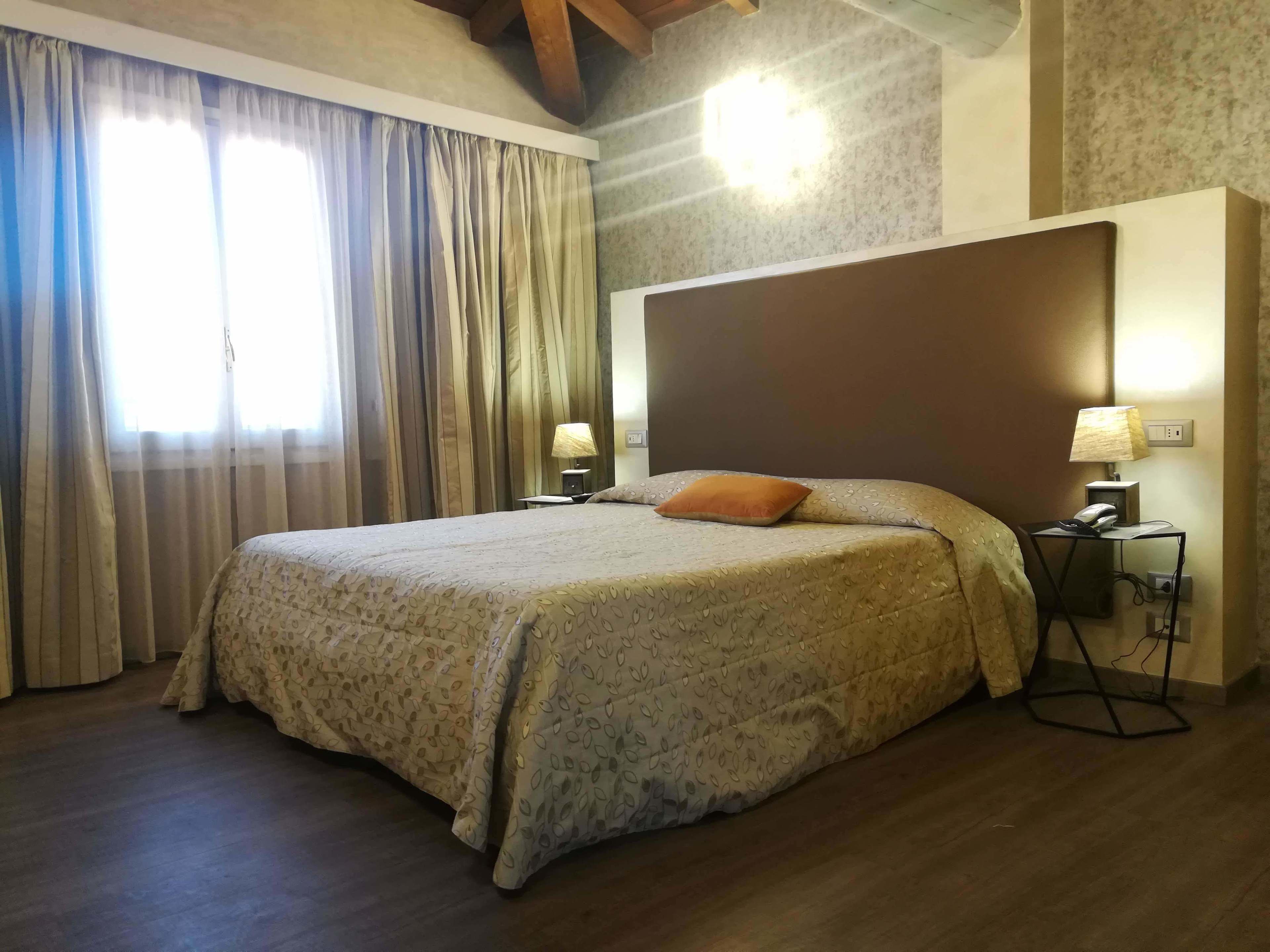 Un lit bien fait, recouvert d’une couvre-lit à motifs, avec deux lampes de chevet et une table de nuit sur laquelle se trouvent un téléphone et une lampe.