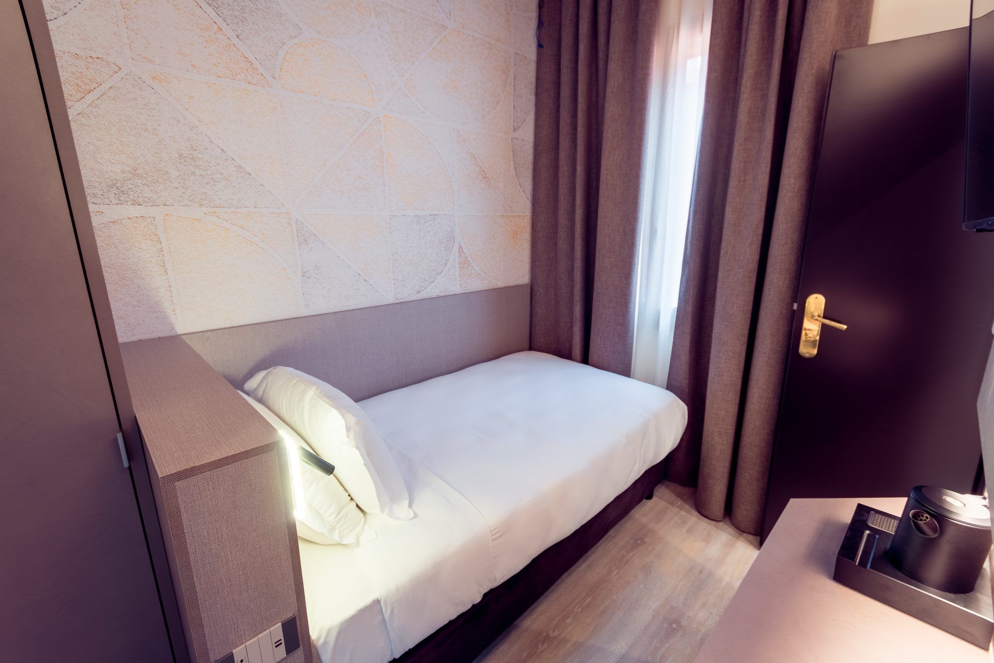 A compact hotel room with a single bed, a small desk, and a door.
