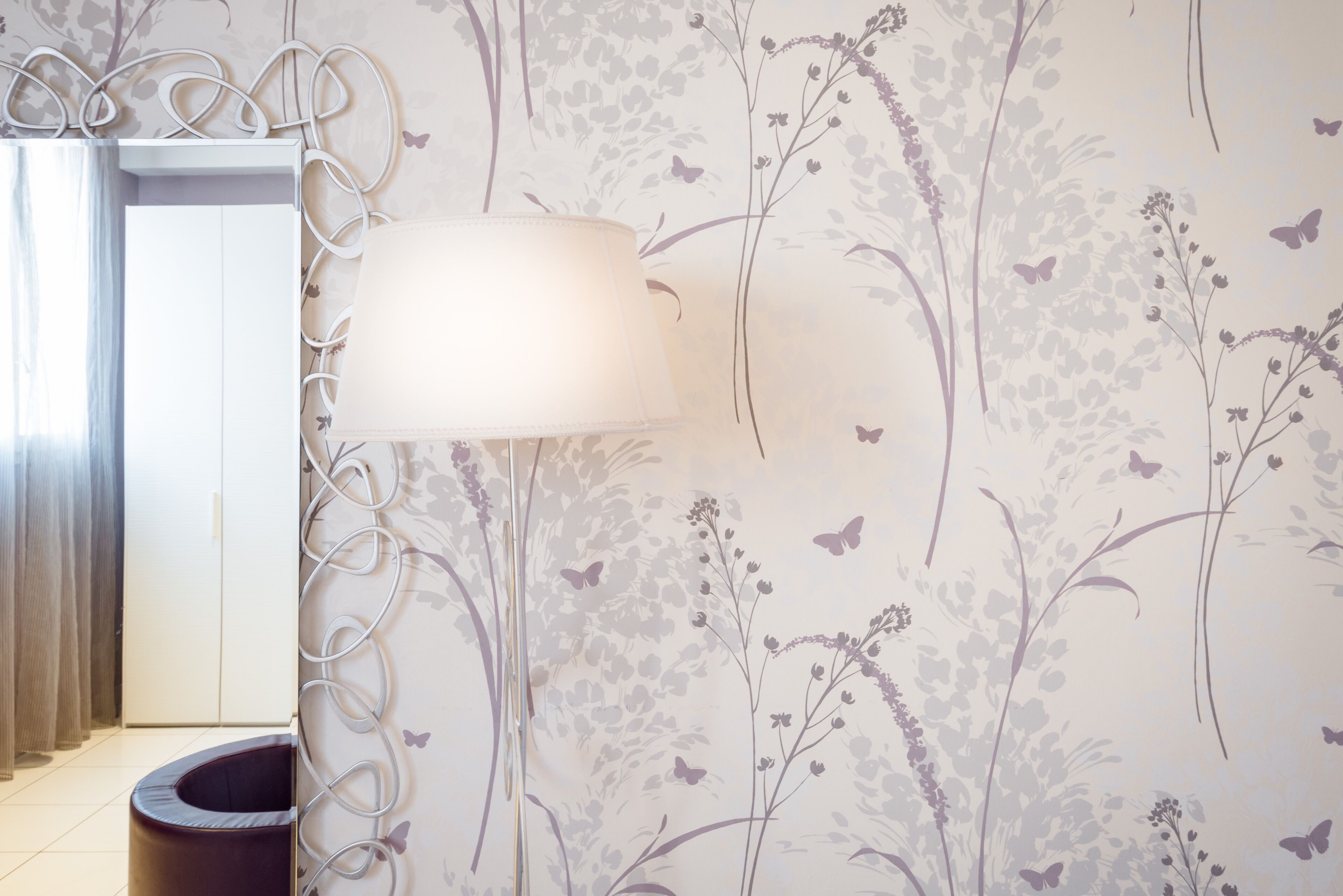 A room with a floral wallpaper, a white cabinet, a black trash bin, and a wall-mounted lamp.