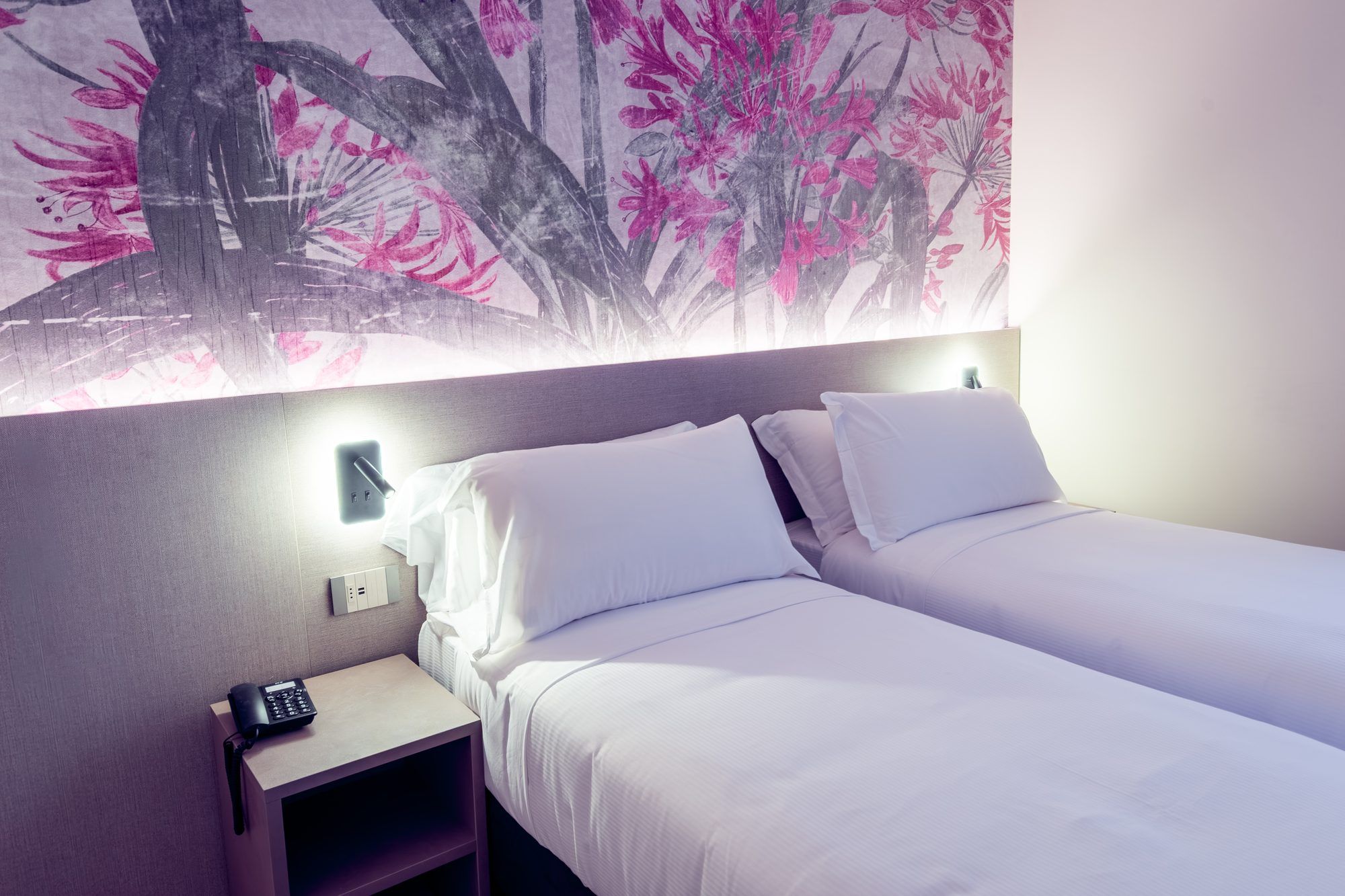 Habitación de hotel con cama, mesita de noche, teléfono y lámpara fijada a la pared.
