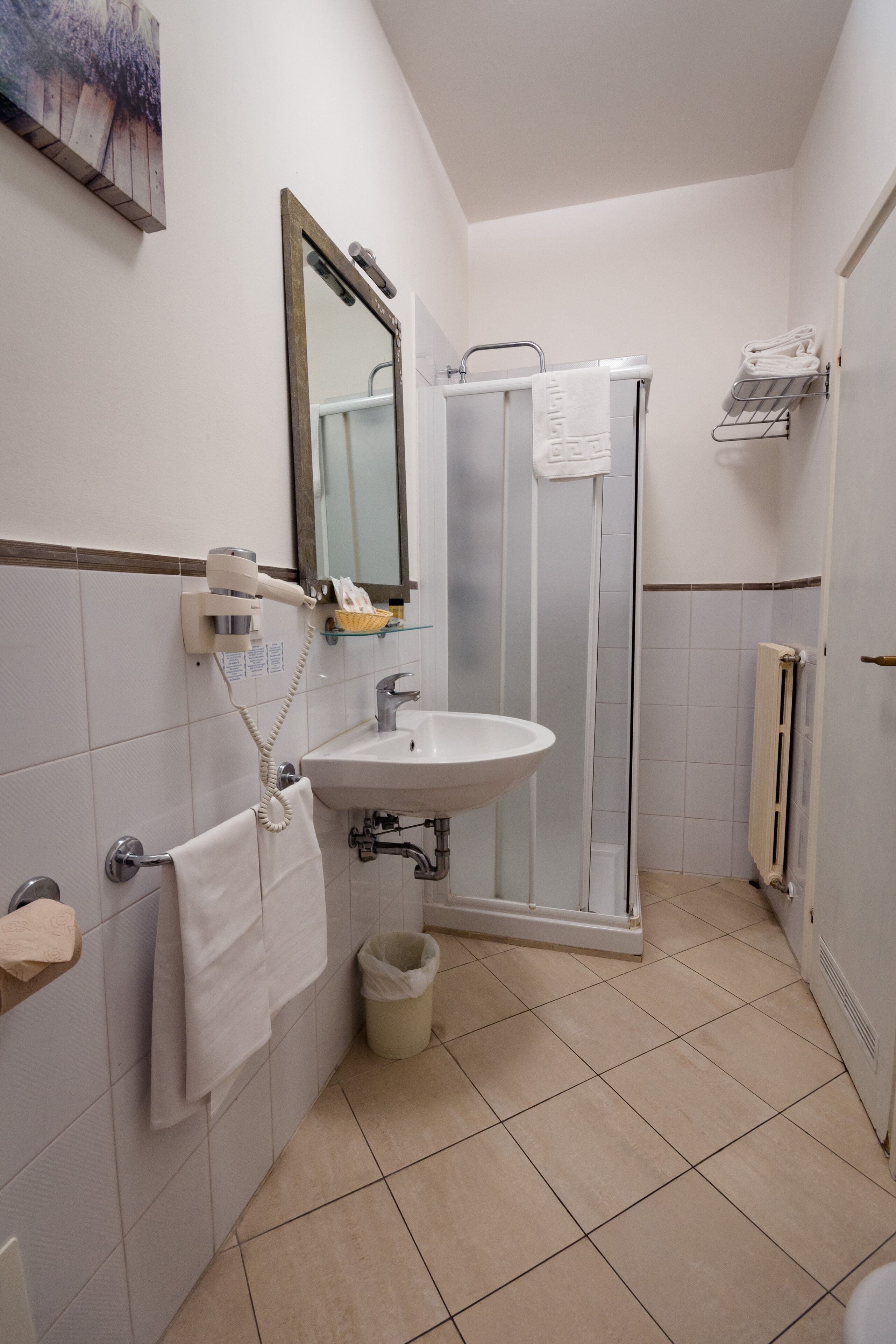 A bathroom with a sink, mirror, towel rack, shower, and a radiator.