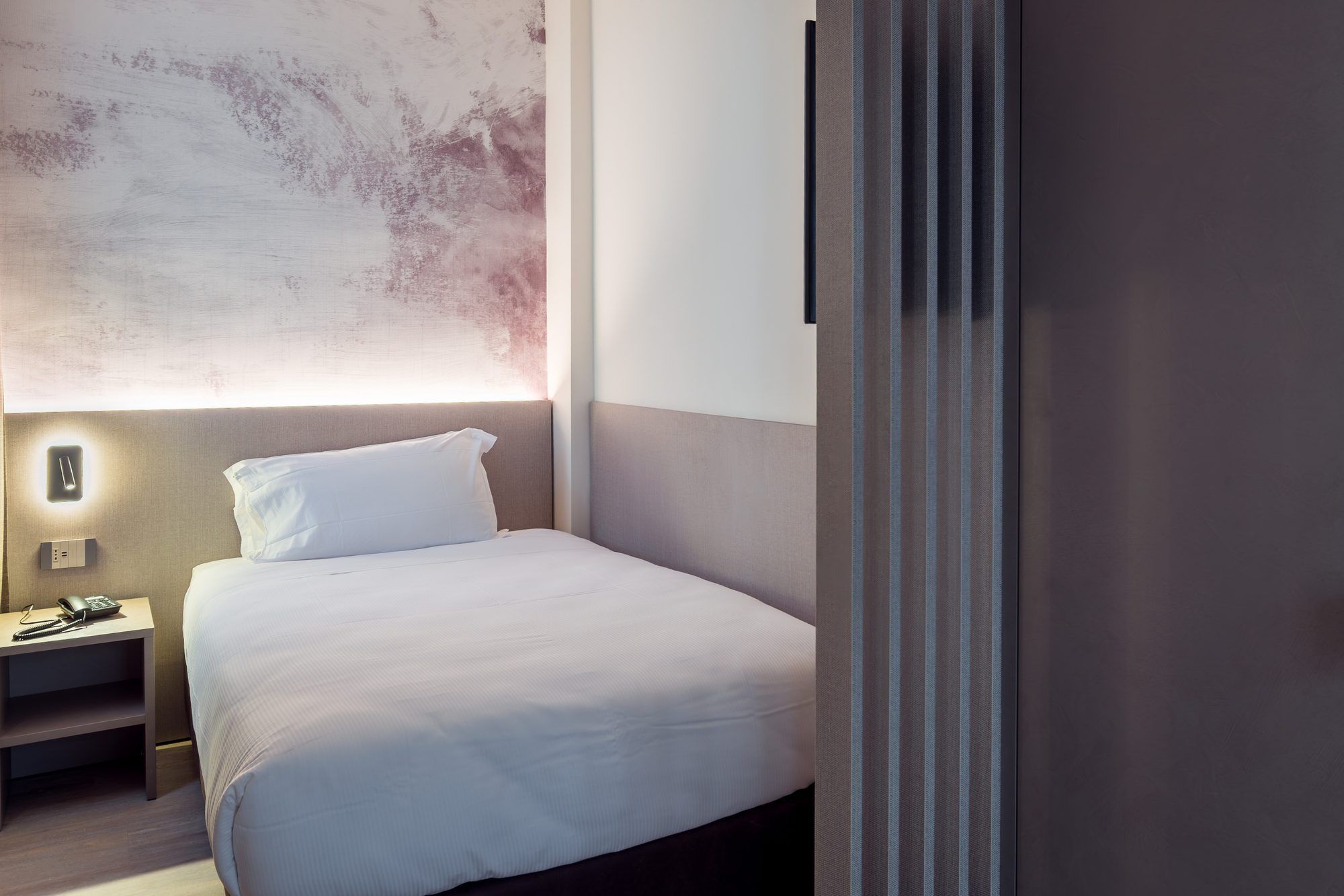 Una habitación de hotel con cama, mesita de noche y lámpara de pared.