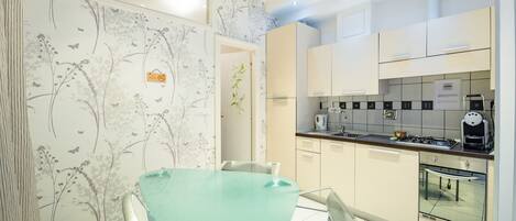 A modern kitchen with white cabinets, a glass dining table, and a floral wallpaper design.