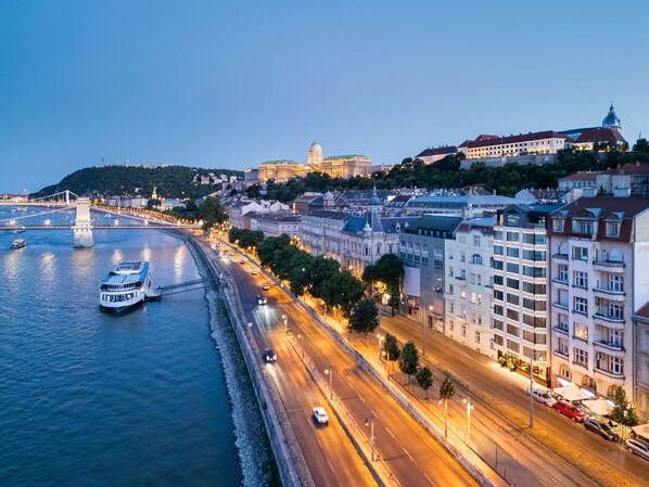 A cityscape with a prominent historic building, a river with a bridge, and a well-lit street with modern buildings.