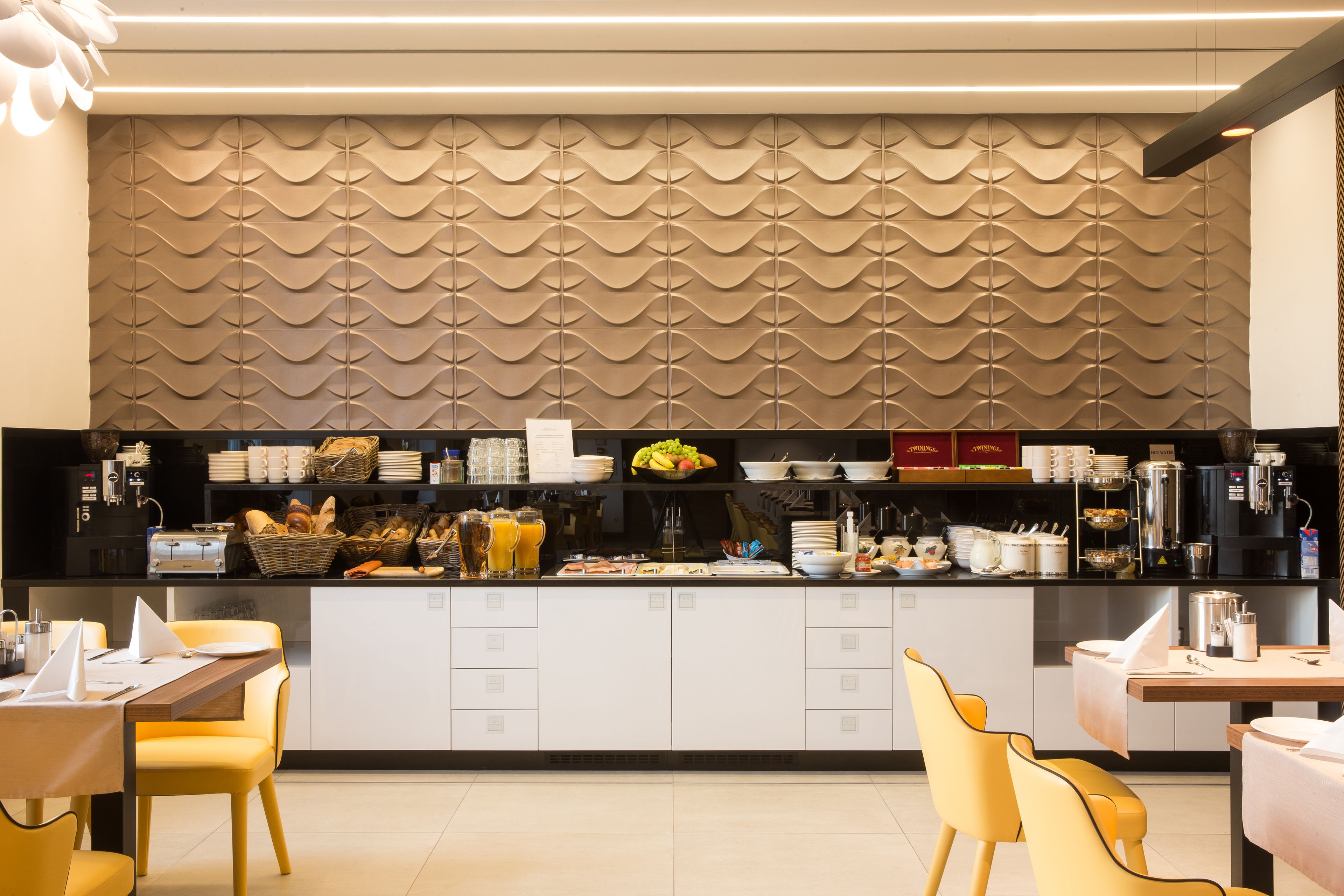 A modern kitchen area with a central island, equipped with various appliances and utensils, and a patterned wall behind the counter.
