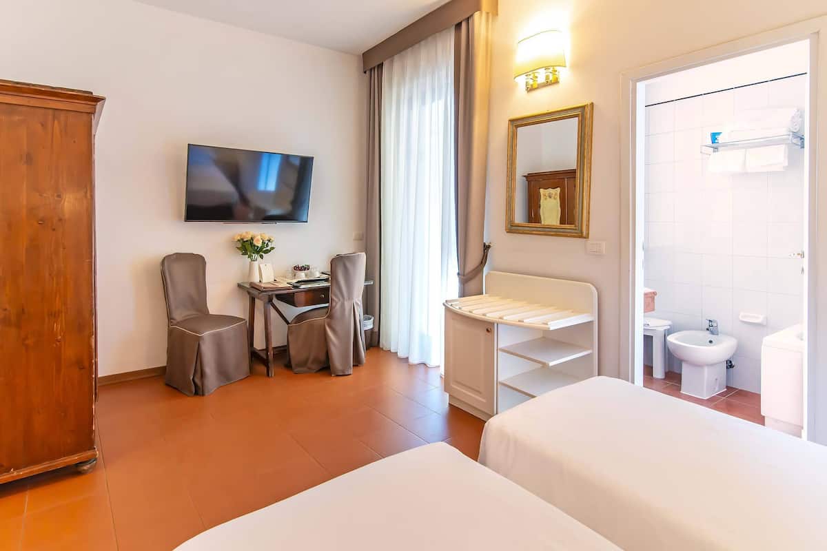 A hotel room with a bed, a desk with a chair, a television, a mirror, and a bathroom with a toilet and sink.