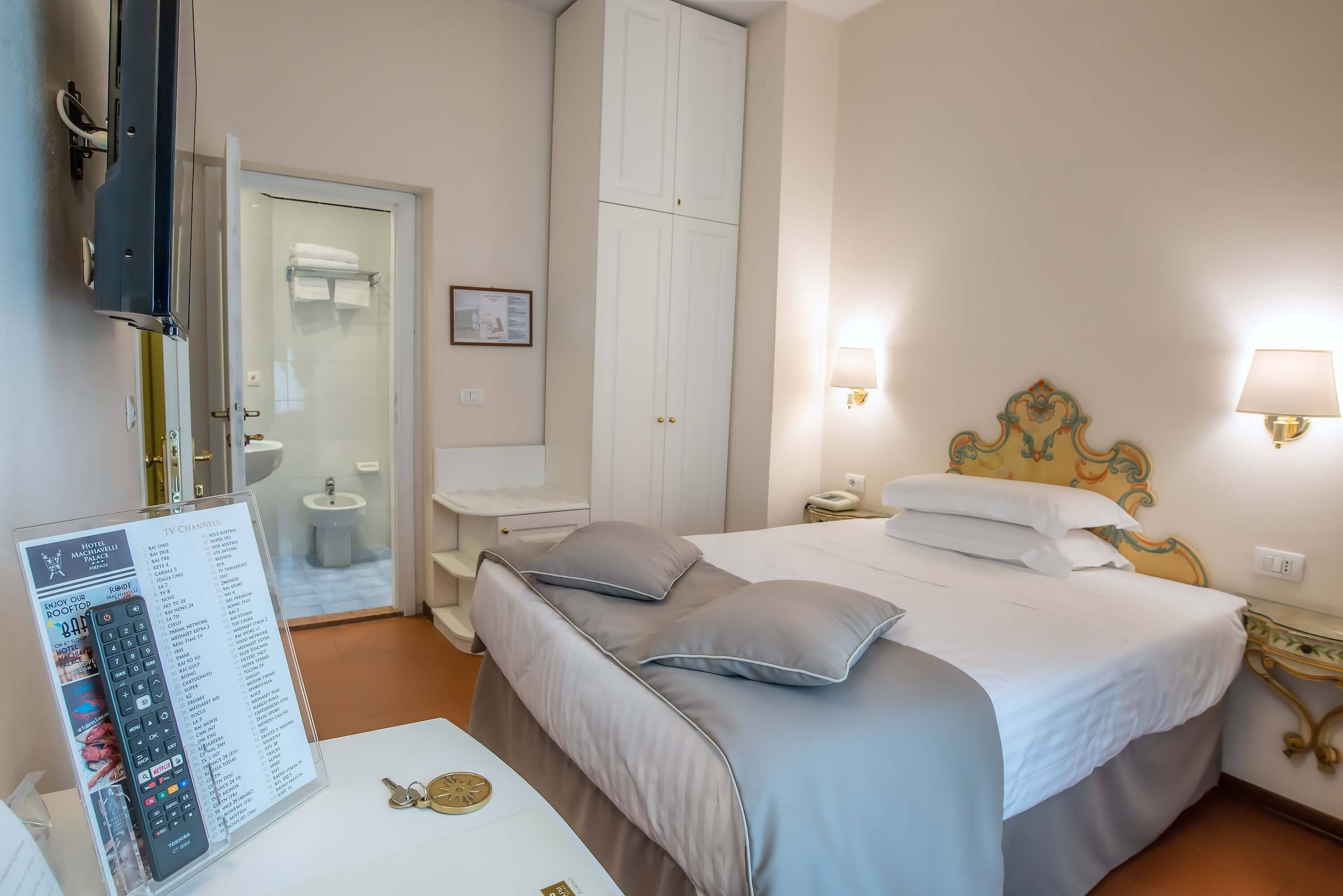Een hotelkamer met een bed, nachtlampjes, een televisie en een badkamer die door een open deur zichtbaar is.