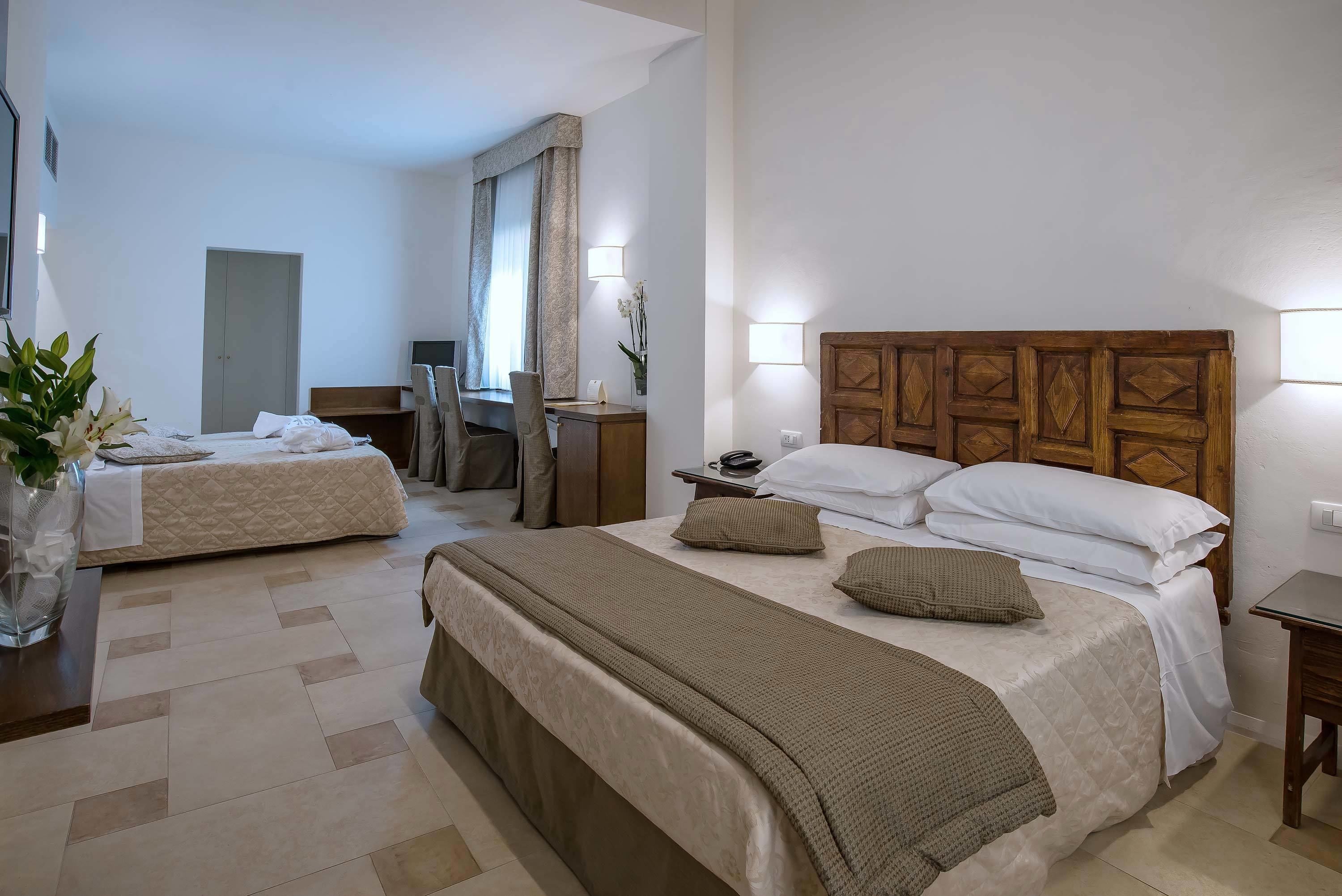 A hotel room with two beds, a desk, a chair, a mirror, and a bedside table with a lamp.