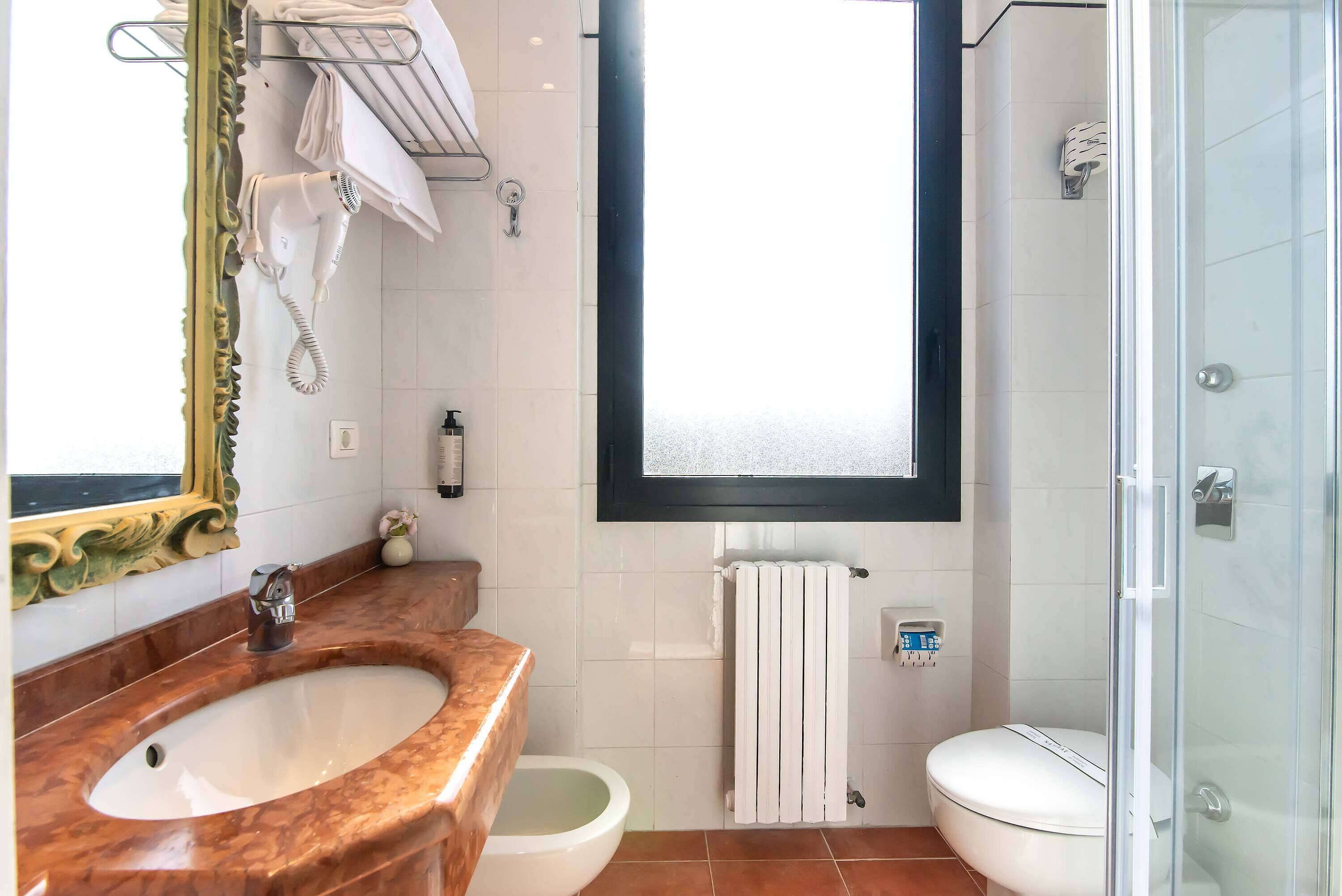 Une salle de bain avec un lavabo en marbre, des toilettes, une douche et un grand miroir.