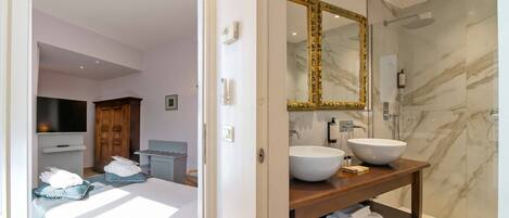 Un baño moderno con un espejo grande, paredes de ducha de mármol y un mueble de tocador de madera con lavamanos blanco.