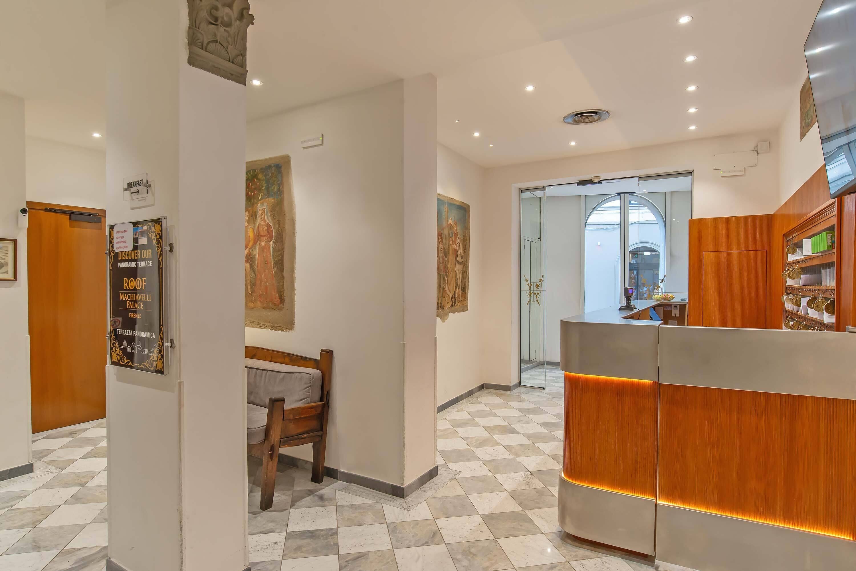 Un vestíbulo de hotel con mostrador de recepción, escritorio de información y una zona de estar con una silla y un banco.