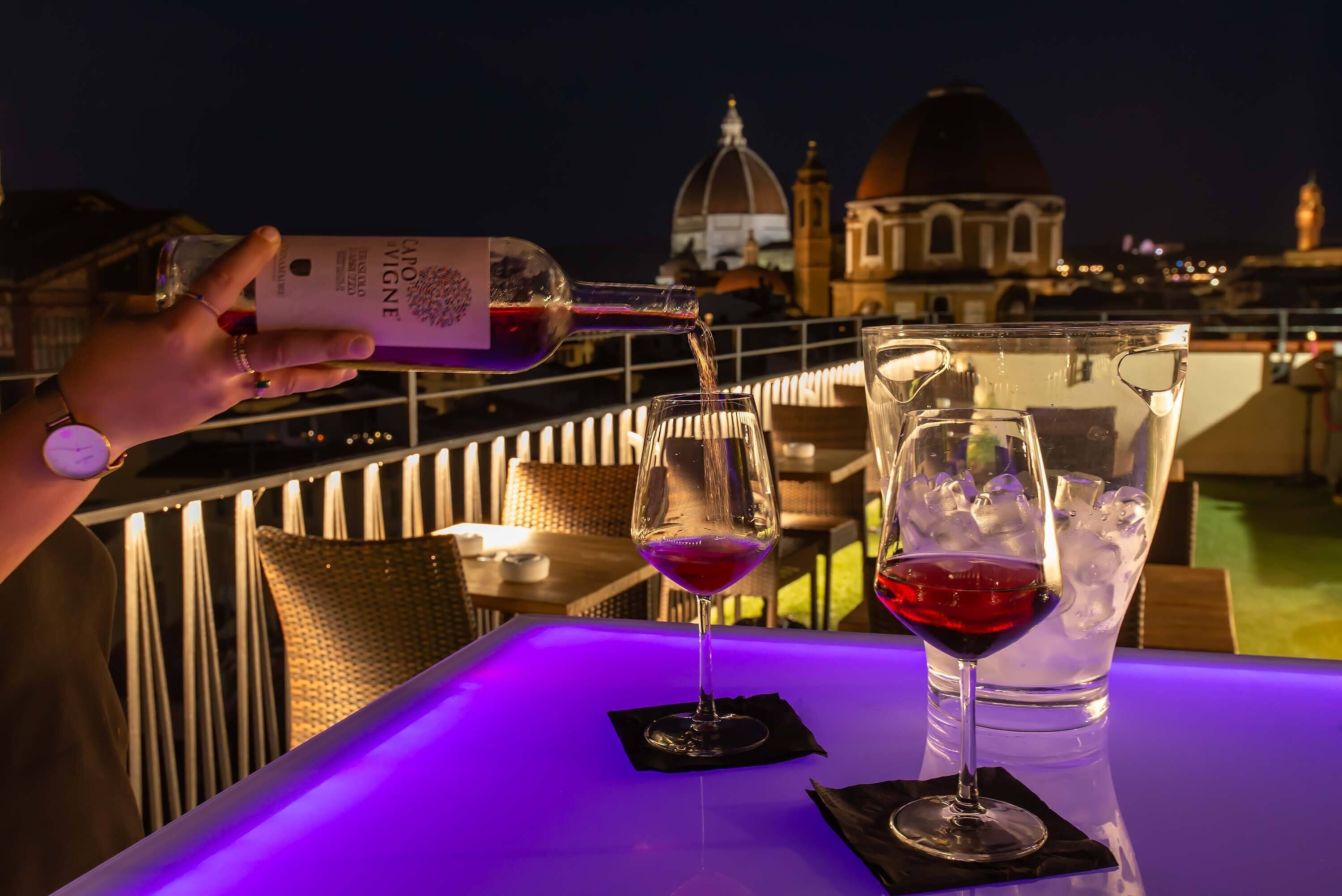 A person pouring wine into a glass on a table with a view of a dome and buildings in the background.