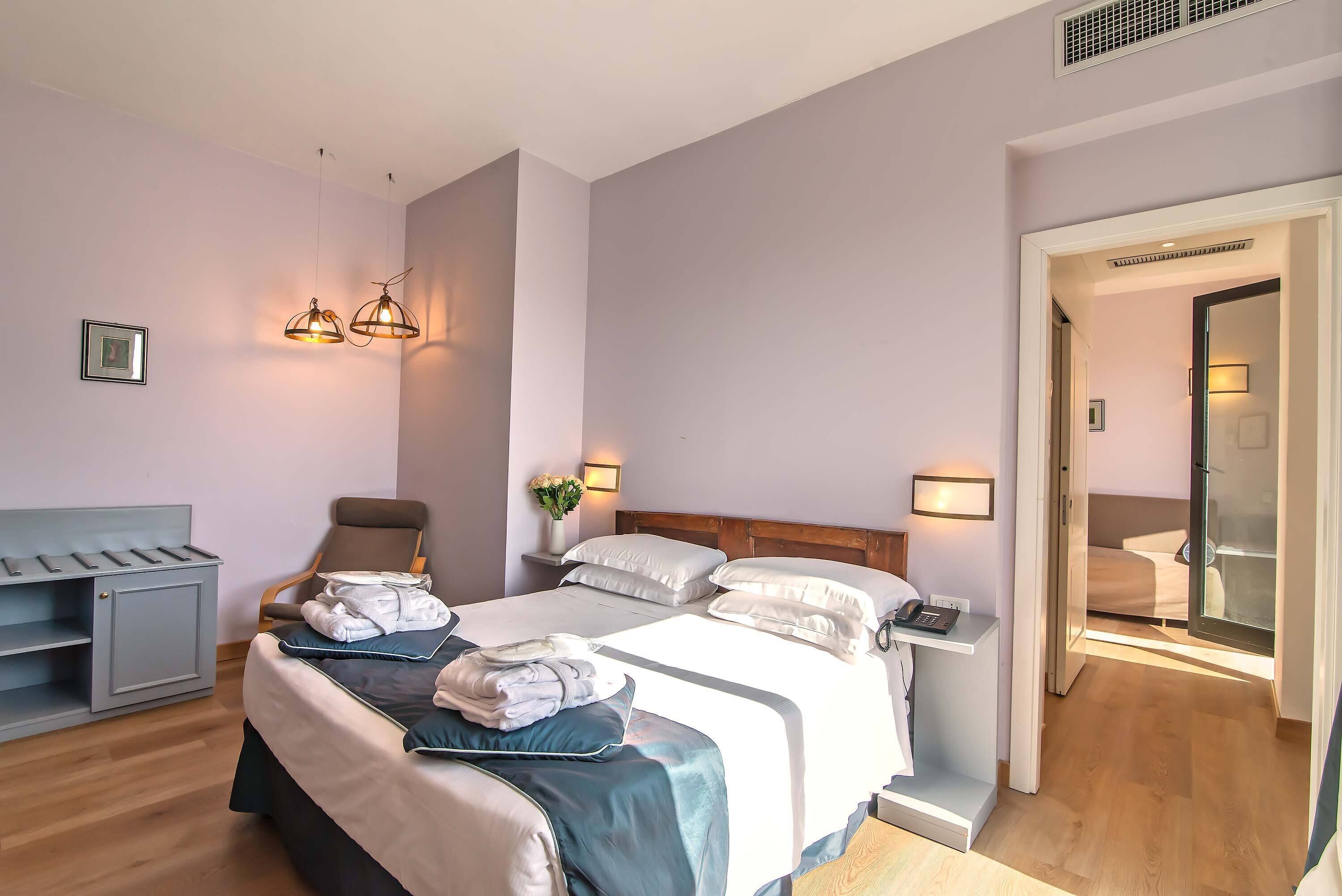 A hotel room with a bed, bedside tables, a chair, a desk, and a wardrobe.