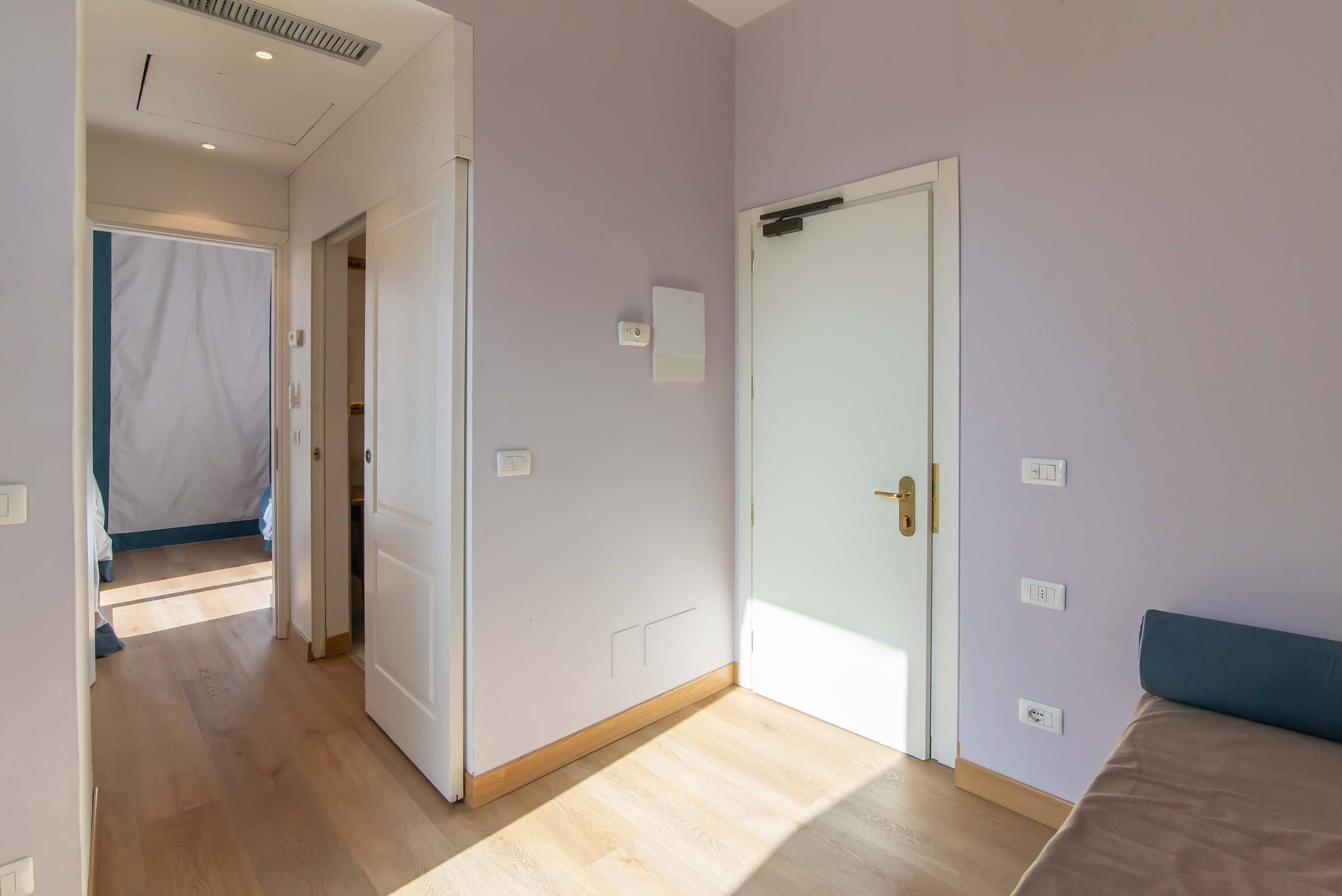 A room with a bed, a door, and a light switch on the wall.