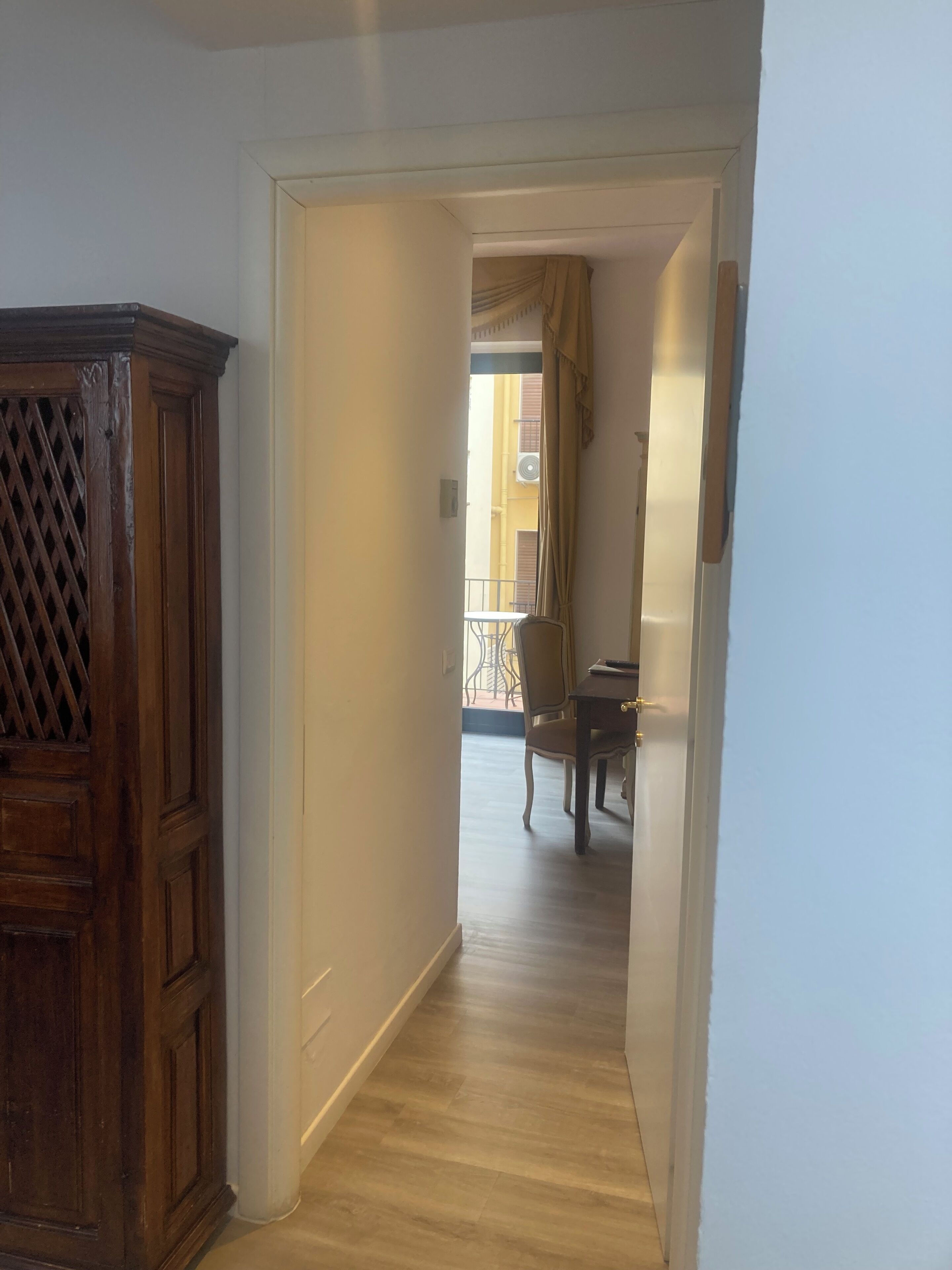 A hallway with a wooden cabinet, a dining area with a table and chairs, and a view of a balcony with a railing.